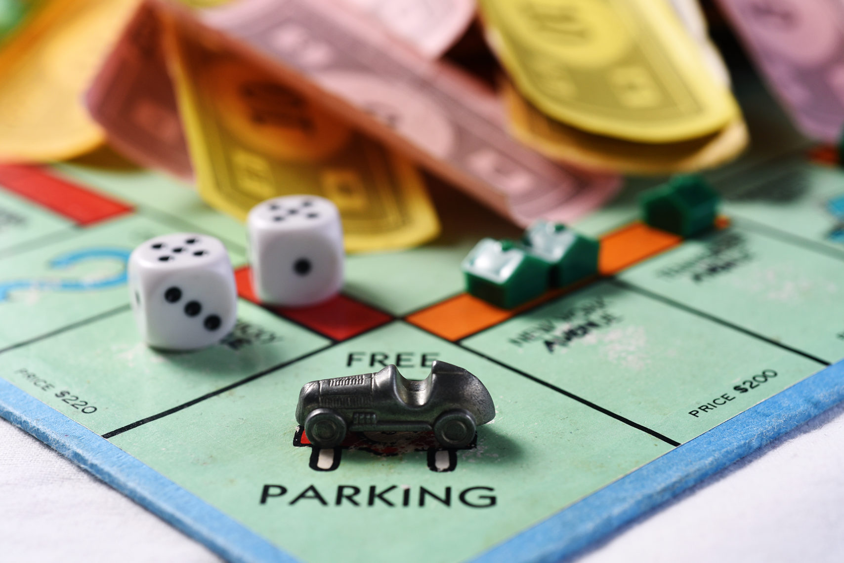 Close up of Monopoly board, Free Parking corner, silver car, dice, Monopoly money