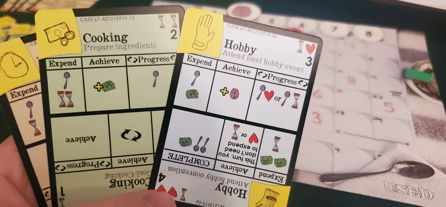 Hand holding three cards from Heading Forward game, "Hobby" card at the front. Game board in background.