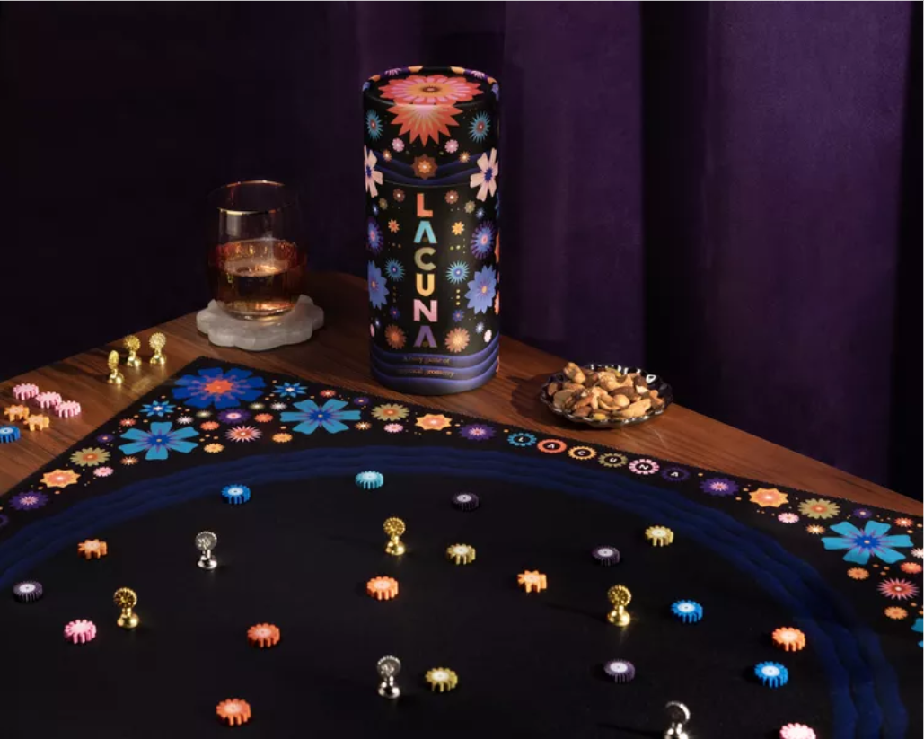 Oblique view of table with Lacuna set up on it: large dark navy circular board with coloured discs and metallic token scattered about.