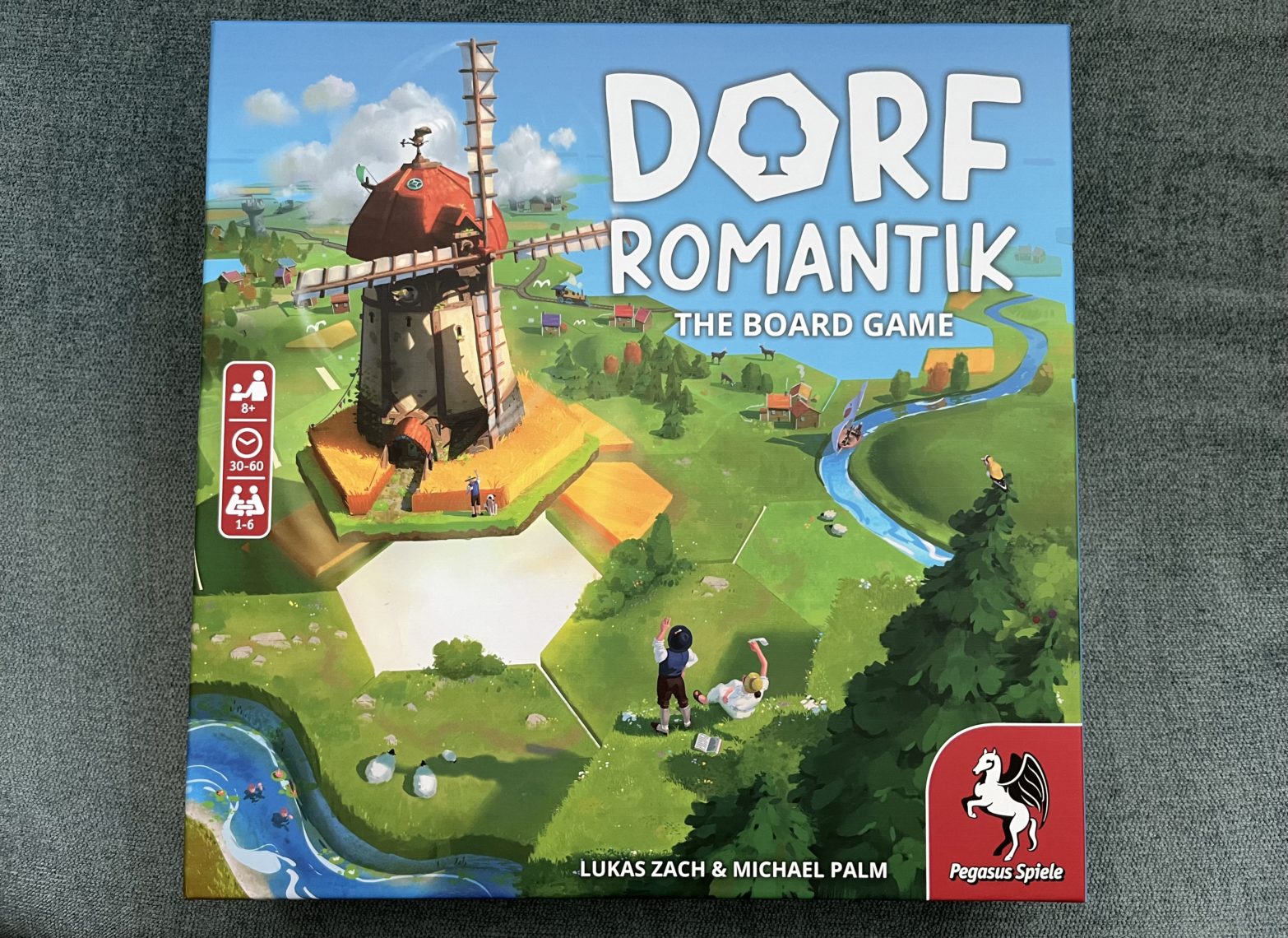 Top-down shot of Dorfromantik: The Board Game against a tourquoise background.